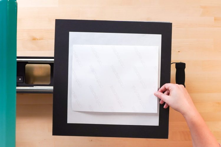 Hands placing a sheet of butcher paper on top to protect the heat press